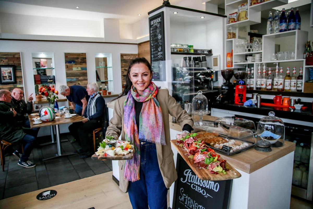 Owner of Café Italissimo poses in cafe holding platters of food